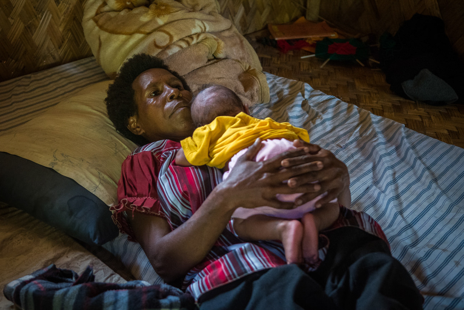 Saviza Community. Henganofi District. A mother holding her baby while in bed.