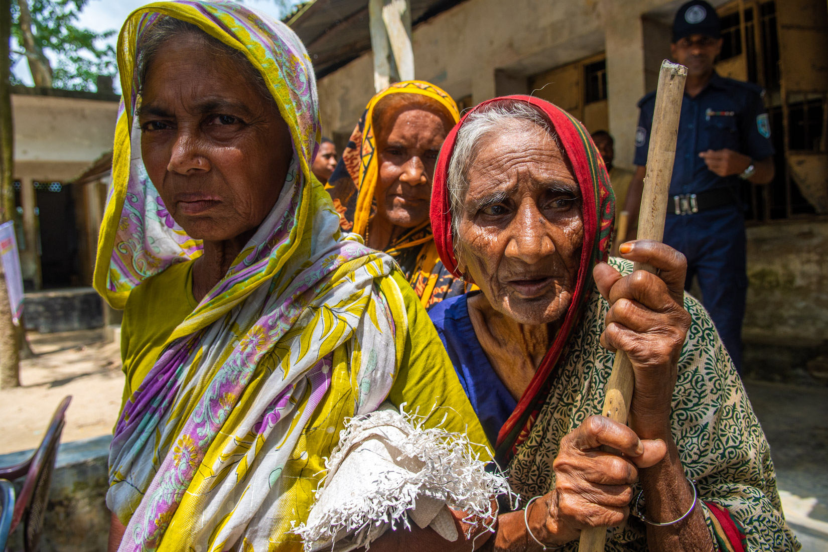 Three old women at the distribution center showing visible signs of angriness, tiredness and frustration.